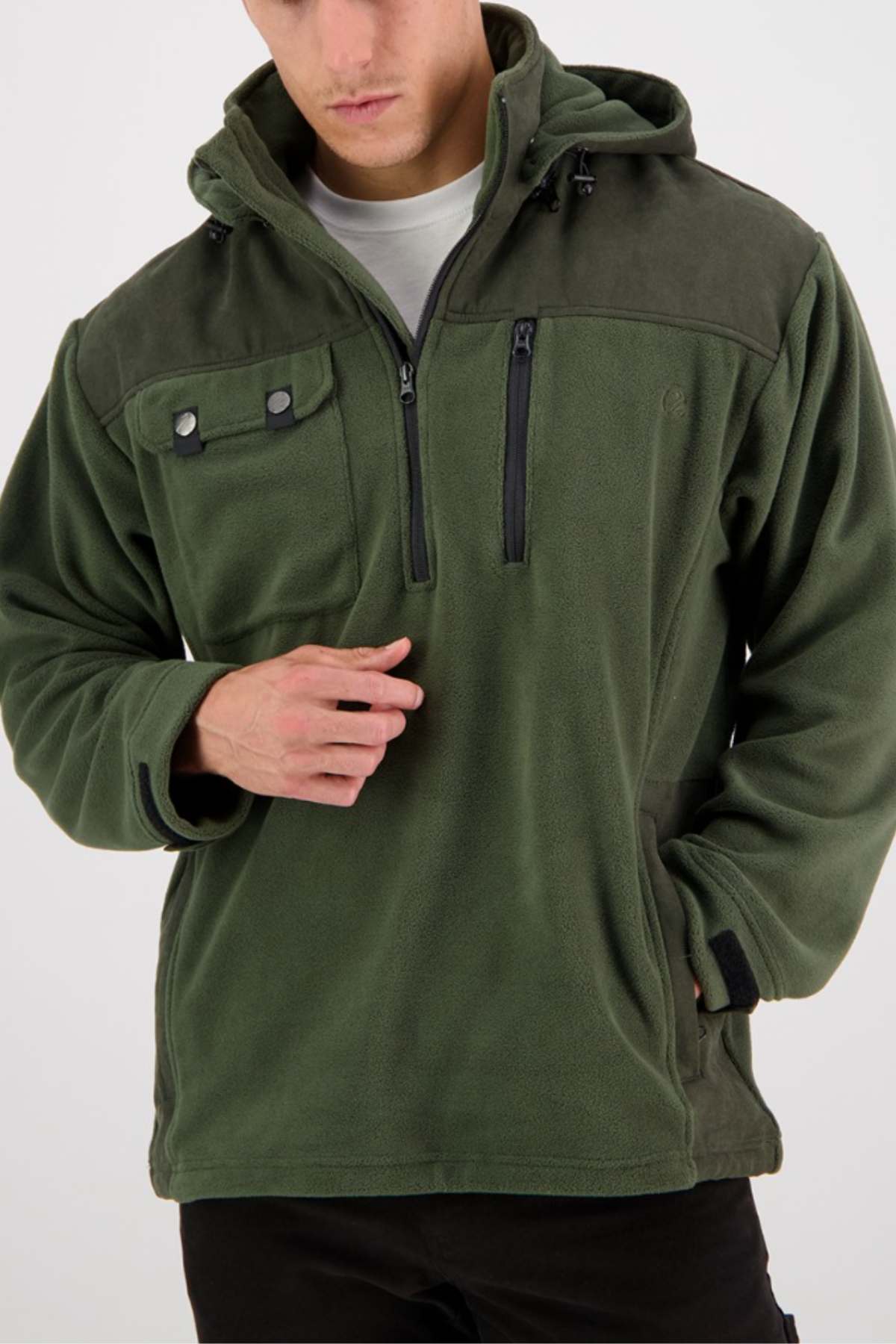 A person wearing a Swanndri High Rock Fleece Pullover in green, featuring a high collar, hood, zip-up chest pocket, two buttoned chest pockets, and side hand pockets. The pullover is made from waterproof fabric. Dressed in black pants and a gray undershirt, the person stands against a plain white background.
