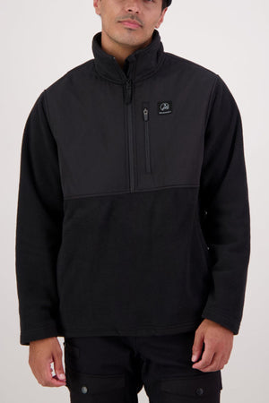 A person wears a black Swanndri High Rock Hybrid Fleece Pullover, made from recycled polyester with a long-sleeve quarter-zip, small zippered chest pocket, and logo patch on the left chest. The background is plain and light-colored.