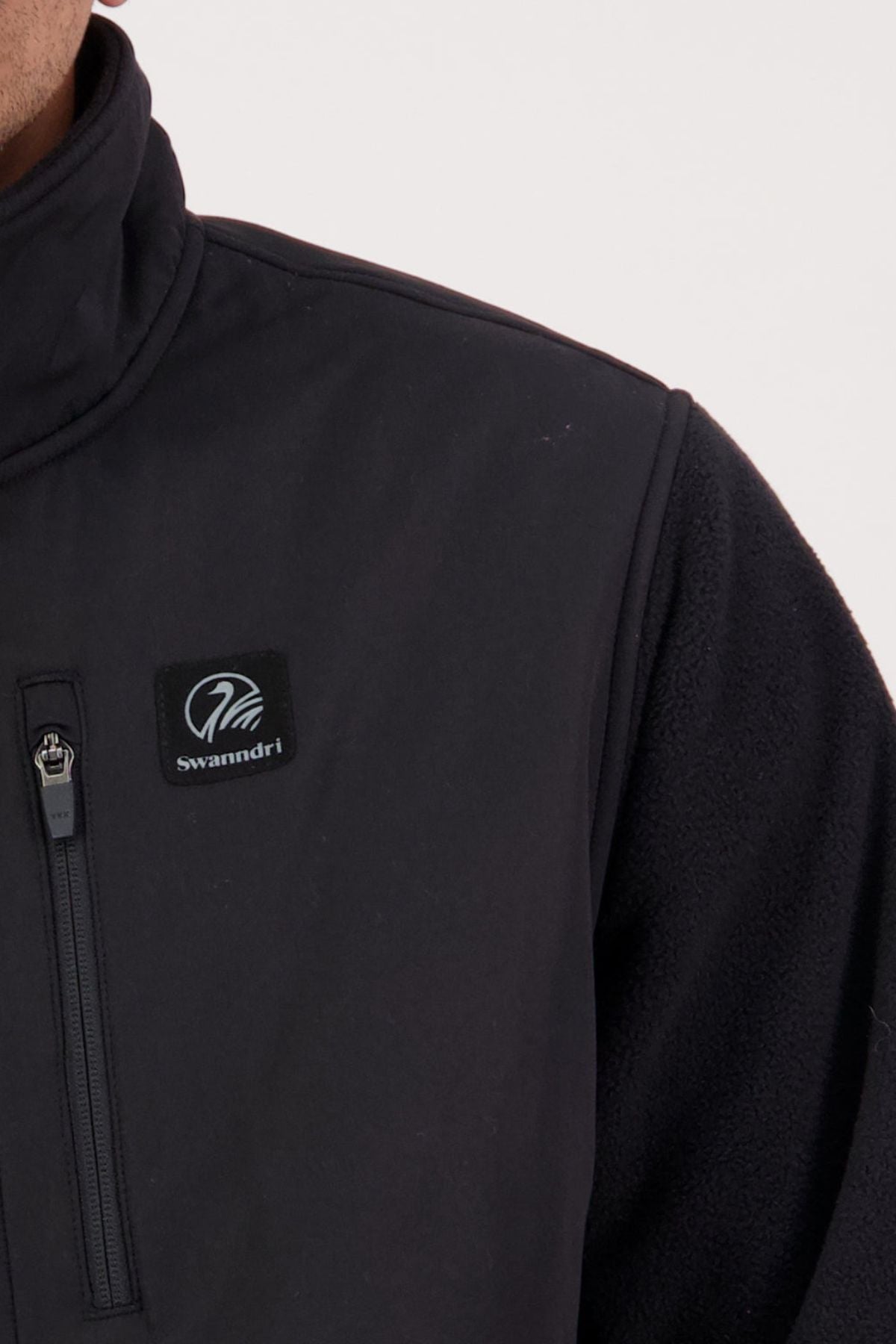 Close-up of a person wearing a black Swanndri High Rock Hybrid Fleece Pullover, made from recycled polyester with a zippered chest pocket and the signature Swanndri logo patch.