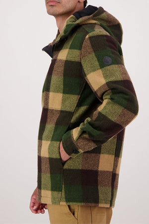 A person stands sideways against a plain background, left hand in the pocket of a green, brown, and tan plaid Swanndri Hudson Hoodie made from New Zealand wool.