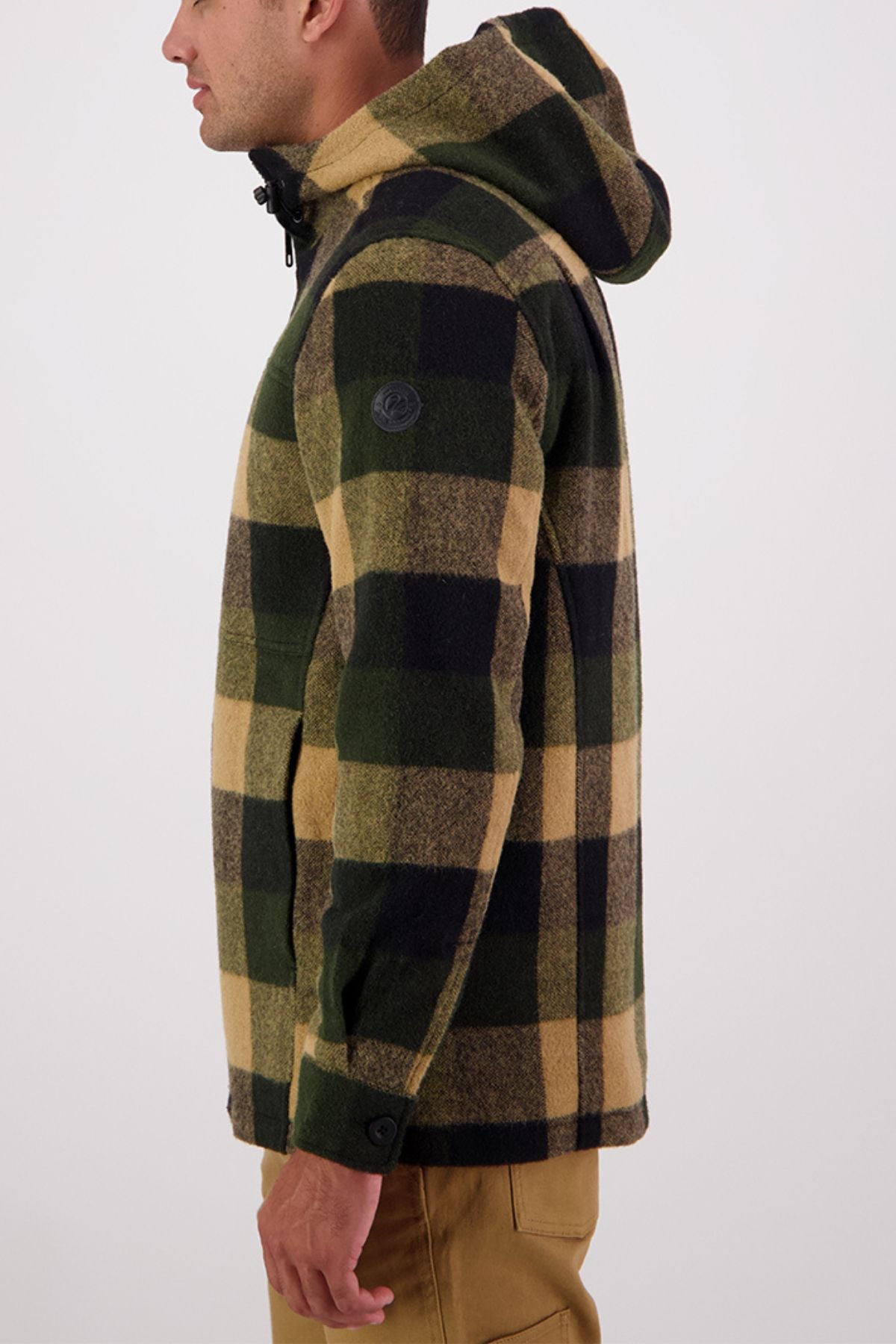 A person in profile, facing left, wears the Swanndri Hudson Hoodie in green, black, and tan plaid with khaki pants against a plain light background. Made from New Zealand wool, this jacket ensures a warm, comfortable fit.