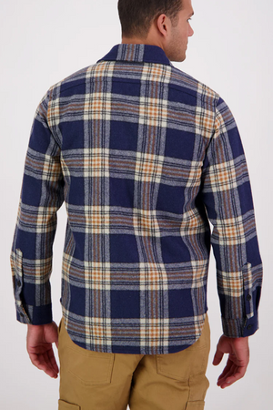 A man is seen from behind wearing a Swanndri Kiaraki v3 Wool Shacket in blue and beige plaid with long sleeves, paired with tan pants, as he stands against a plain light background.