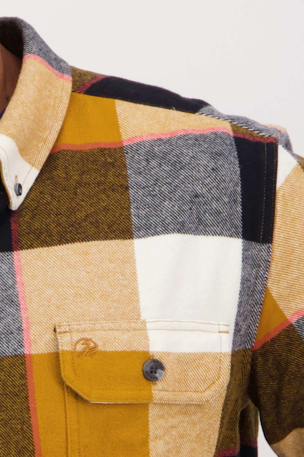 A close-up of the Swanndri Lowcliffe Shacket highlights a classic fit plaid shirt with large yellow, black, red, and white squares. Made from 100% cotton, it has a textured look, front pocket, black button, and a partially visible collar hinting at timeless style.