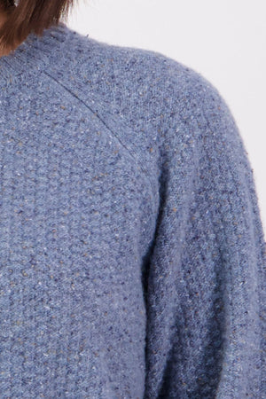 Close-up of a person wearing the Swanndri Lyttelton Womens Waffle Crew in light blue lambswool. The textured sweater features raglan sleeves; only the shoulder, upper chest, and part of the neck are visible against a plain background.