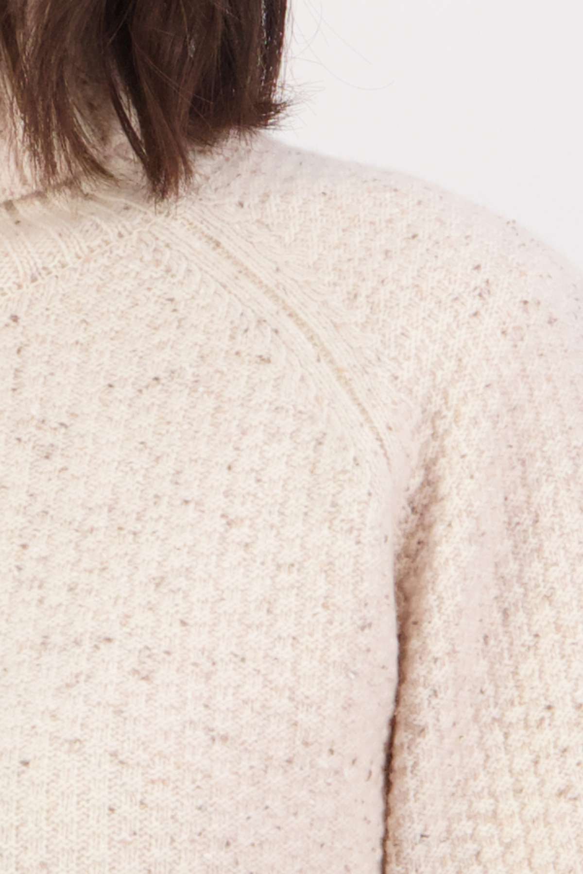 Close-up of a person wearing the Swanndri Lyttelton v2 Roll Neck Knit, a cream-colored jumper with a Donegal tweed-inspired textured pattern. Their hair is visible at the top of the image.