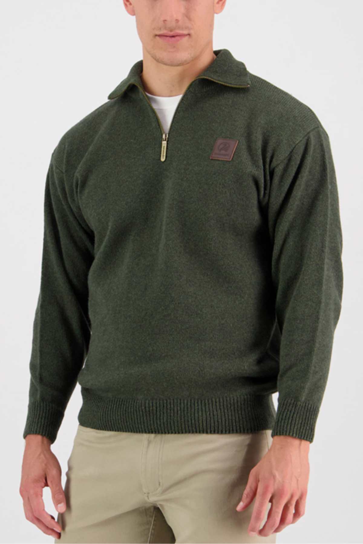 A man is wearing a Swanndri Mariner Zip Neck Sweater in dark green wool blend, featuring a logo on the left chest area. He has a white shirt underneath and is dressed in beige pants. The background is white.