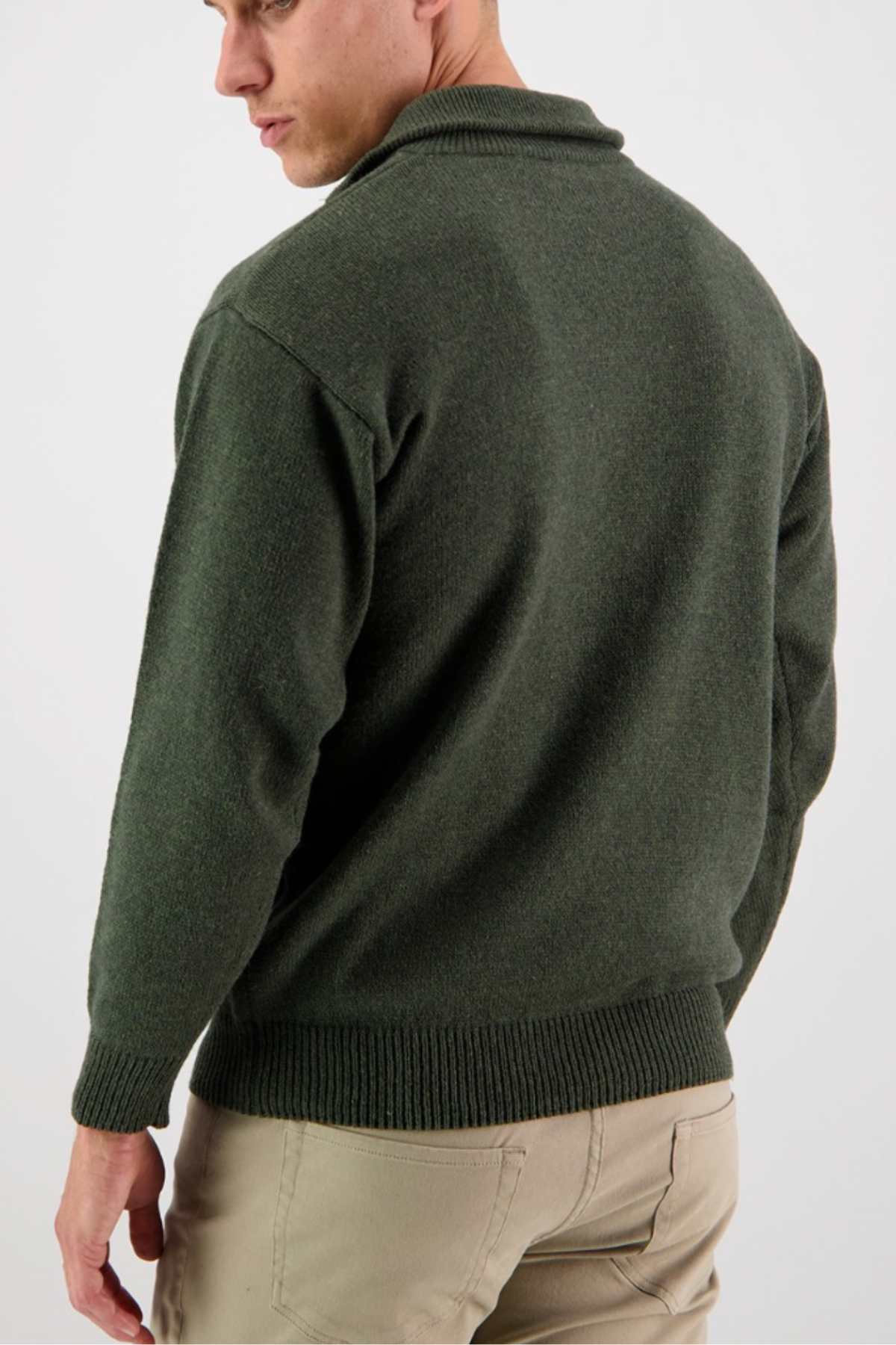 A person is shown from the back, wearing a Swanndri Mariner Zip Neck Sweater in olive green wool blend with a collar and light beige pants. The image focuses on the upper body, highlighting the texture and fit of the knit sweater. The background is plain and light-colored.