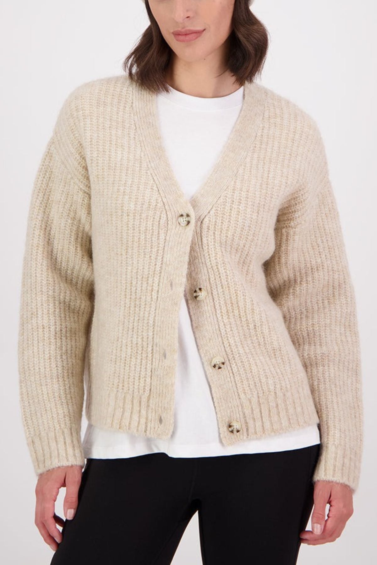 A woman wears the Swanndri Marydale Cardigan in cream over a white tee and black pants, standing against a plain white background. This sustainable mohair wool blend cardigan is stylish and eco-friendly.
