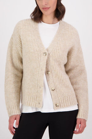 A woman wears the Swanndri Marydale Cardigan in cream over a white tee and black pants, standing against a plain white background. This sustainable mohair wool blend cardigan is stylish and eco-friendly.