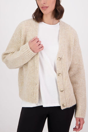 A woman models the Swanndri Marydale Cardigan—a cream, chunky mohair wool blend—over a white tee and black pants, standing against a plain light background and holding the cardigan open for an effortless, sustainable look.