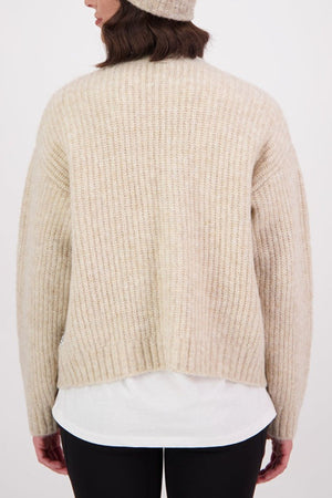 A person is shown from the back against a plain white background, wearing the Swanndri Marydale Cardigan—a beige mohair wool blend sweater—paired with a matching beanie, white shirt underneath, and black pants for an effortless sustainable look.