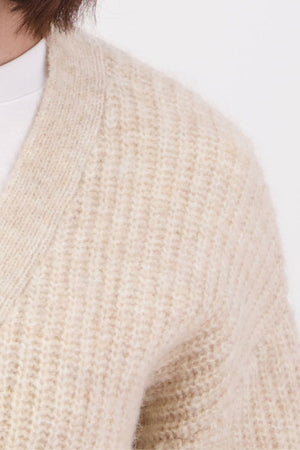 Close-up of a person wearing the Swanndri Marydale Cardigan in a cream-colored, textured knit mohair wool blend over a white shirt; only the shoulder, chest, and neck are shown against a plain background.