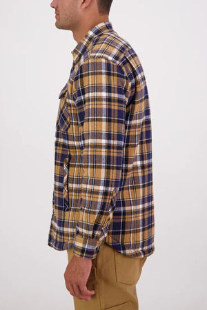 A man stands in profile against a plain light background wearing a Swanndri Morven Sherpa Long Sleeve Shirt—100% cotton in brown, navy blue, and white plaid—paired with khaki pants.