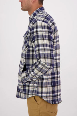 A man in a blue and white plaid Swanndri Morven Sherpa Long Sleeve Shirt stands in profile with his hands in the pockets of his tan pants against a plain light background.
