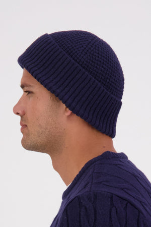 A man in profile wears the Swanndri Newton Beanie with a matching dark blue waffle knit sweater, set against a plain light background.