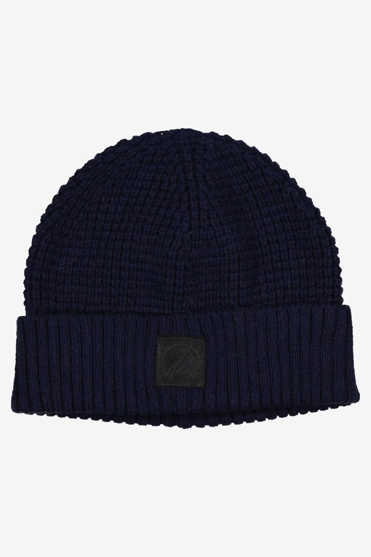 The Swanndri Newton Beanie is a dark blue waffle knit hat with a folded brim and a small black rectangular patch on the front, shown laid flat on a plain white background.