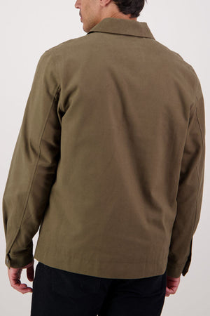 A man is shown from the back wearing the Swanndri Northgate Canvas Jacket in olive green and black pants against a plain, light background.