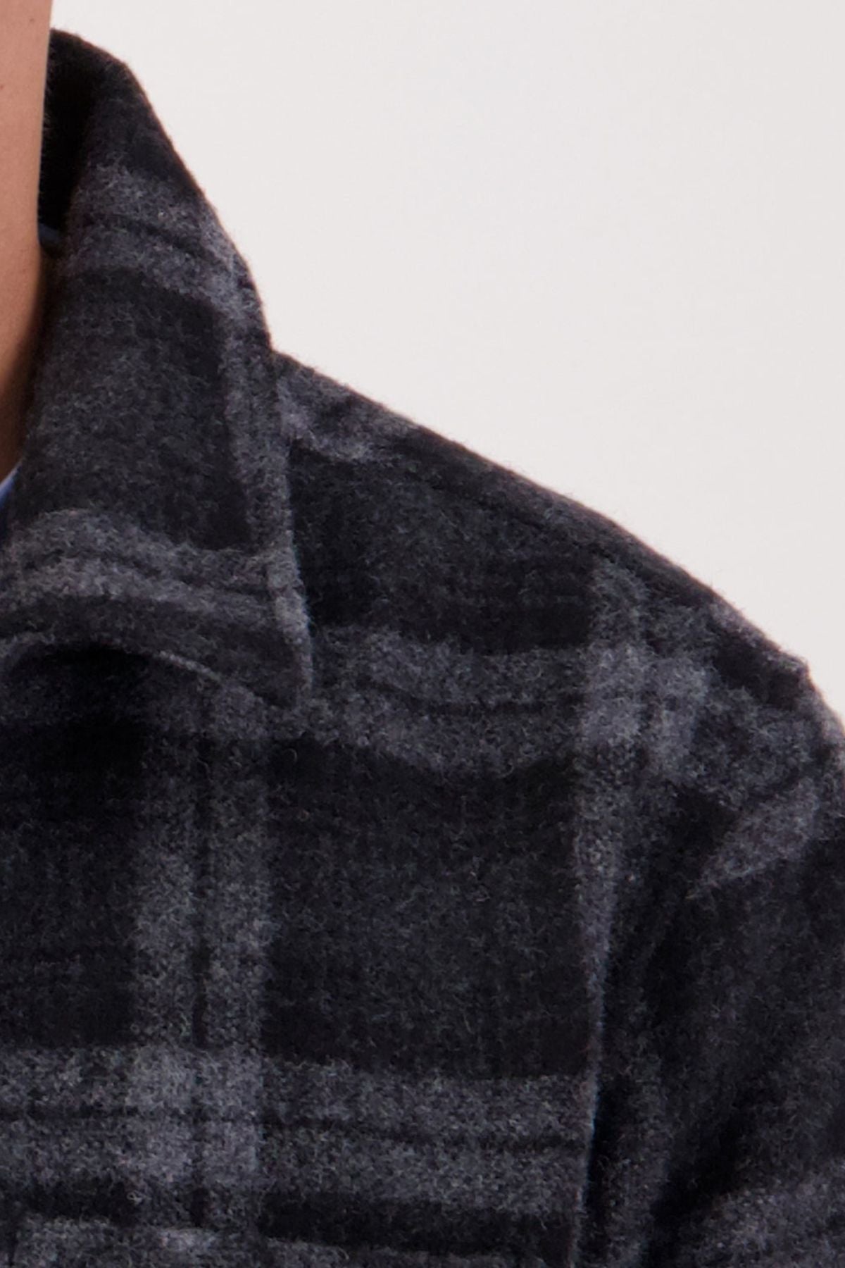 Close-up of a person wearing the Swanndri Northgate V2 Jacket in dark gray plaid, made from premium New Zealand wool, featuring a collar. The image focuses on part of the shoulder, collar, and neck against a plain light background.