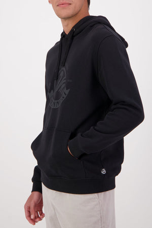 Wearing the Swanndri Original V2 Hoodie—a black cotton polyester sweatshirt with a subtle logo and front pocket—paired with light pants, a person stands against a plain background, face partially out of frame.