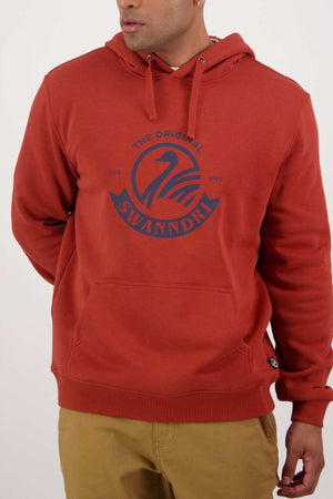 A person is wearing a rust-colored Swanndri Original V2 Hoodie, featuring an abstract swan logo, with a front pocket and drawstrings, along with tan pants.