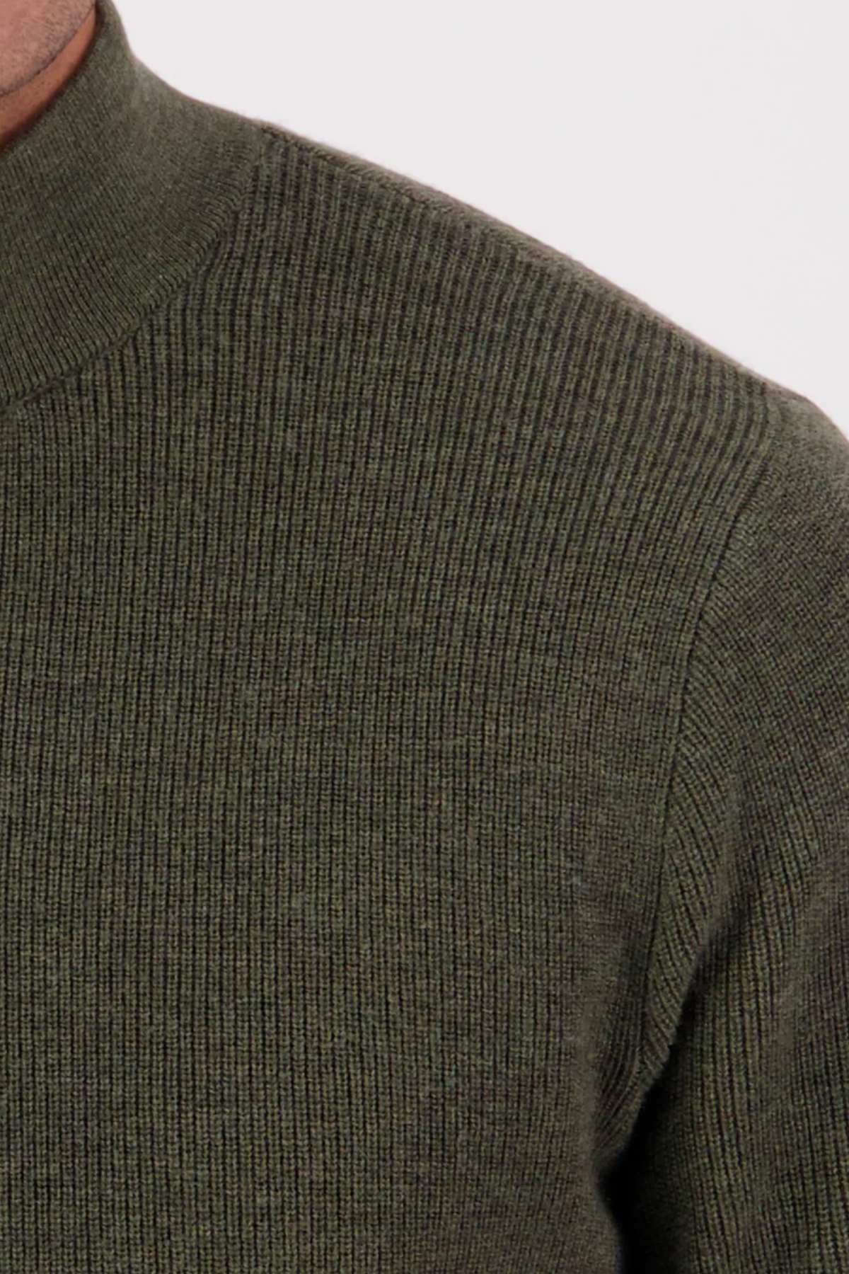 Close-up of a person wearing the Swanndri Otahu River Quarter Zip Merino Knit in olive green, showing only the upper shoulder and part of the chest against a plain, light background.