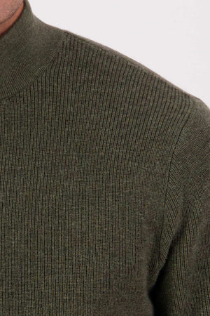 Close-up of a person wearing the Swanndri Otahu River Quarter Zip Merino Knit in olive green, showing only the upper shoulder and part of the chest against a plain, light background.