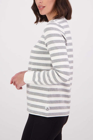 A woman stands sideways against a plain background in the Swanndri Papamoa Stripe Long Sleeve Tee and black pants. Her face is partly out of frame, emphasizing the tee's relaxed fit, maximum comfort, and effortless style.