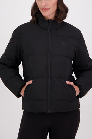 A woman with shoulder-length wavy hair, her face partially visible, stands against a plain white background wearing the Swanndri Plume Down Jacket with a full zip front and her hands in the pockets.