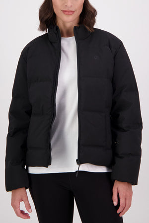 A person wears a black Swanndri Plume Down Jacket made from Polyester 100D Oxford, slightly open over a white t-shirt and black pants, standing against a plain light background with their face partially visible.