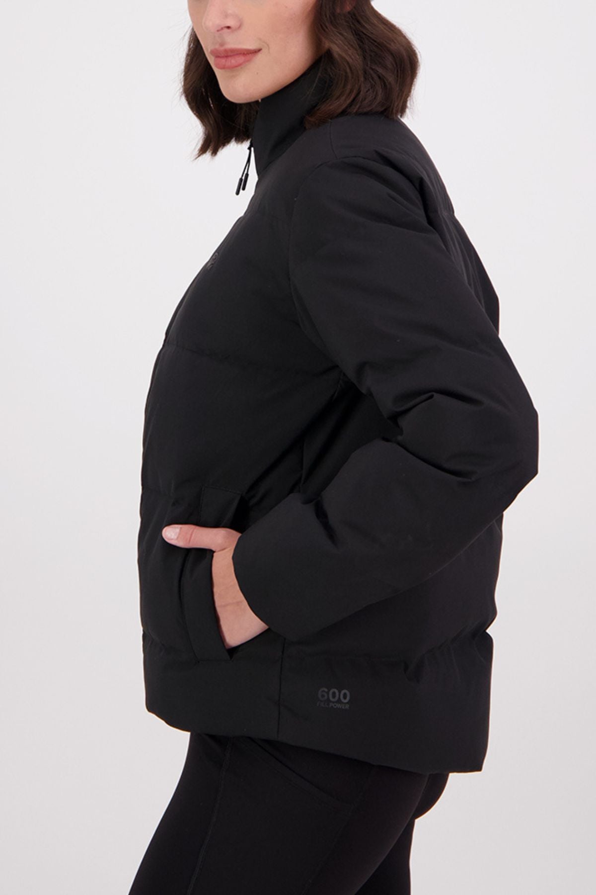 A woman, shown from the side against a plain white background, has her hand in the pocket of a Swanndri Plume Down Jacket with a full zip front, high collar, and 100D Oxford polyester fabric.