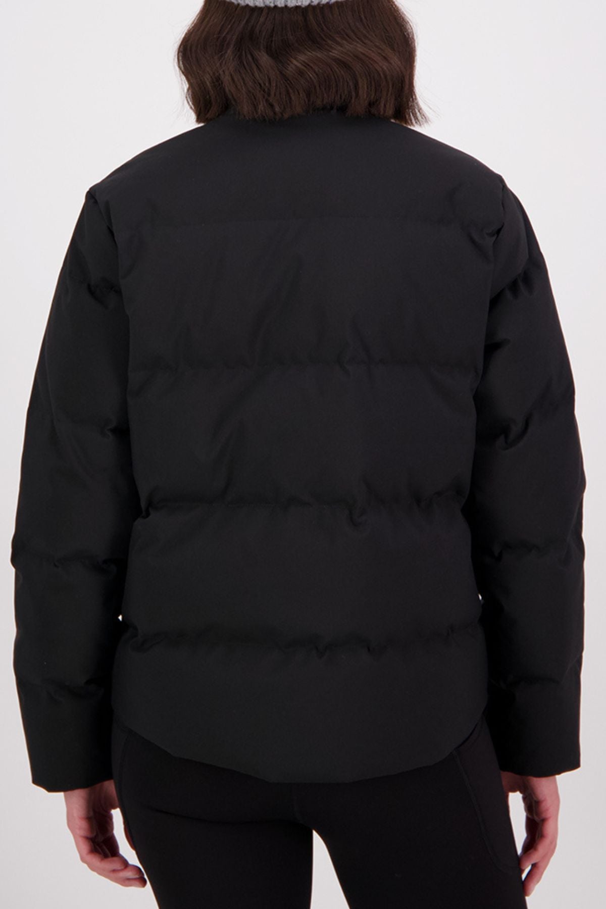 A person with shoulder-length dark brown hair is shown from the back wearing a black Swanndri Plume Down Jacket and black pants, standing against a plain white background.
