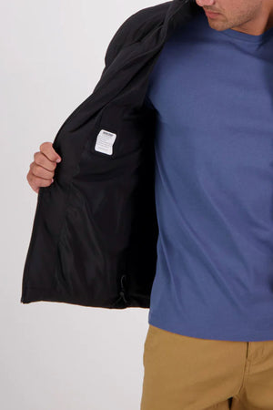 A person in a blue shirt and tan pants holds open a Swanndri Plume Mens Down Jacket, revealing its interior lining and white tag. The person's face is partially out of frame. This jacket is insulated with Duck Down, making it perfect for outdoor use.