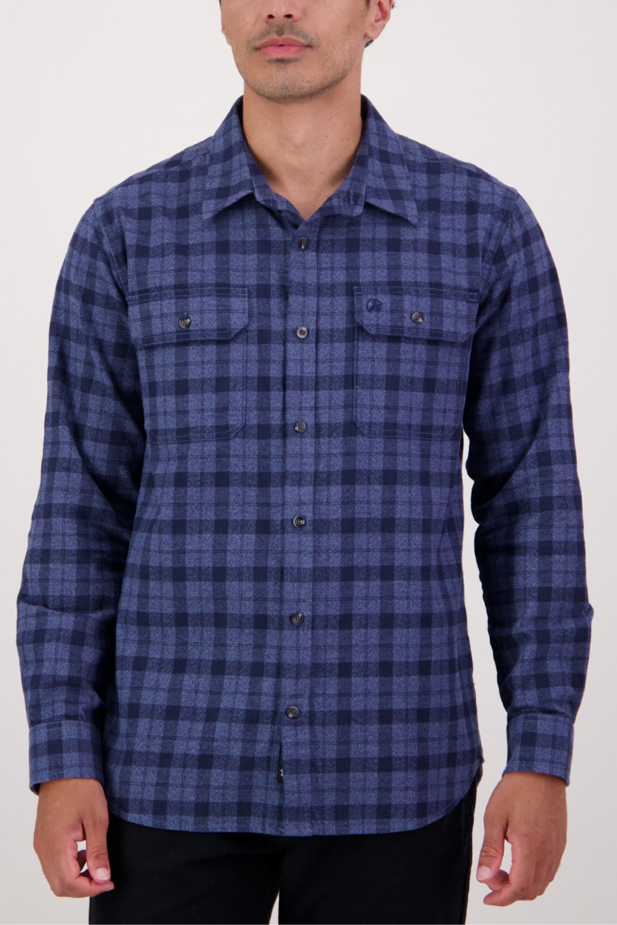 A man wearing a Swanndri Port Road Shirt—a heavy weight, long-sleeve blue and black check shirt with two chest pockets—stands against a plain light background.