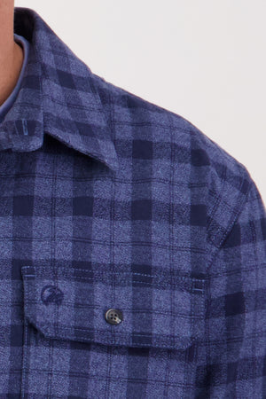 Close-up of a person wearing the Swanndri Port Road Shirt in blue and navy, made from heavy weight twill with a buttoned chest pocket and collar. Only part of the neck and shoulder are visible against a plain background.