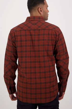 A person faces away from the camera wearing a Swanndri Port Road Shirt, a long-sleeved red and black checkered cotton shirt with buttoned chest pockets, a collar, and buttoned cuffs. It is perfectly paired with sleek black pants.
