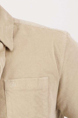 Close-up of the Swanndri Ranfurly Corduroy Shirt in beige, highlighting the upper left section with a button-down collar and front pocket. The heavy weight cotton fabric features fine vertical ridges, and there is a subtle logo embroidered on the pocket, all contributing to its tailored fit.