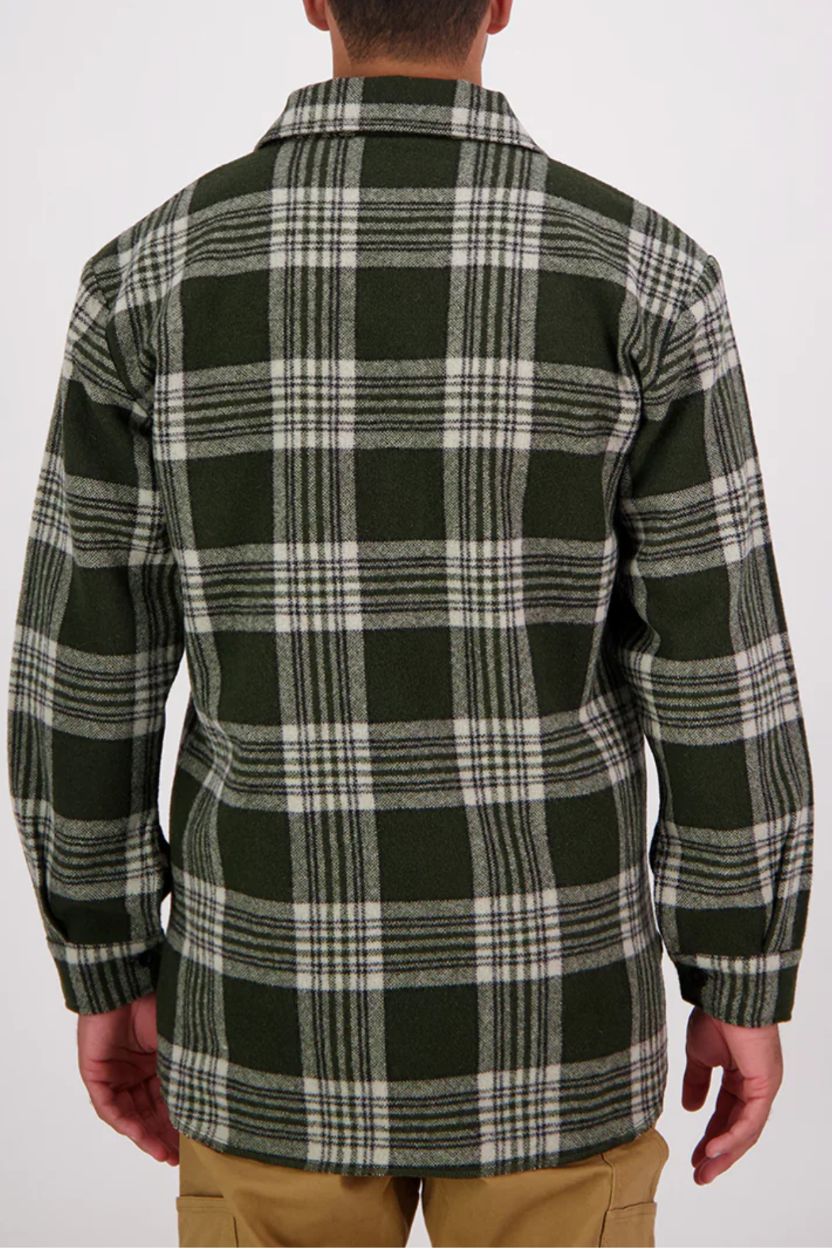 A person wearing a green, white, and black Swanndri Ranger Bush Shirt with an oversized plaid design stands facing away from the camera. The long-sleeve shirt is paired with tan pants against a plain white background.