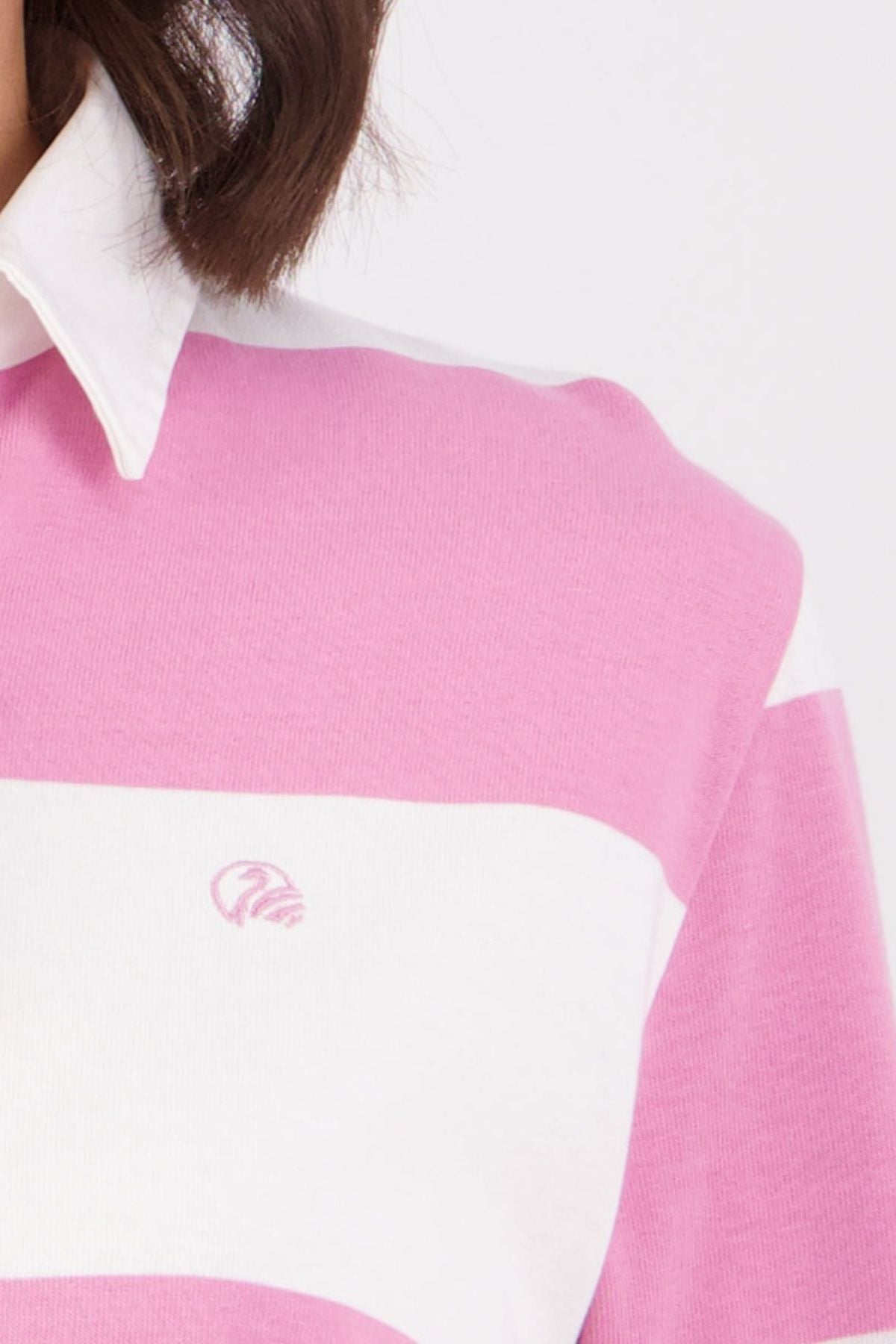 A close-up of a person with chin-length brown hair wearing a pink and white striped Swanndri Ridgeway Womens Rugby shirt, made from 100% cotton, featuring a small embroidered logo on the chest.