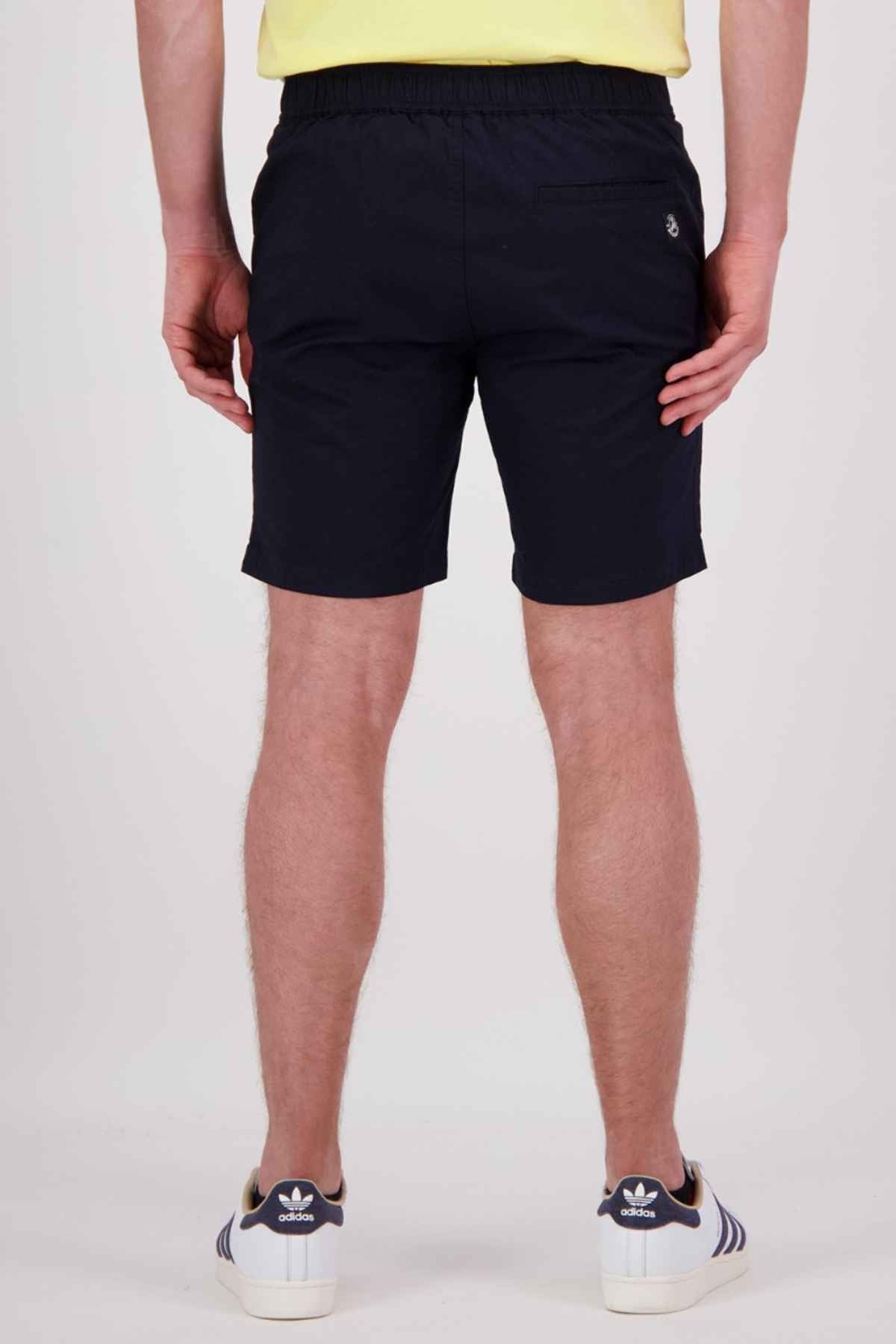 Rear view of a person wearing a yellow shirt, Swanndri Sandy Point shorts in black with multiple pockets, and blue Adidas sneakers with white stripes, standing against a plain light background.