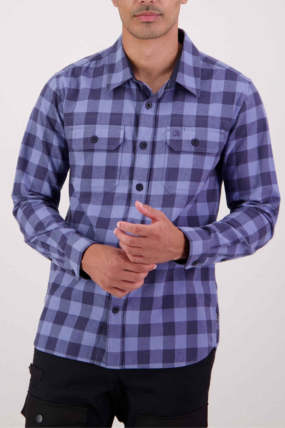 A person wears a long-sleeve Swanndri Taranaki Tailor Shirt in blue and purple plaid, made from 100% cotton with buttoned chest pockets, standing against a plain light background.