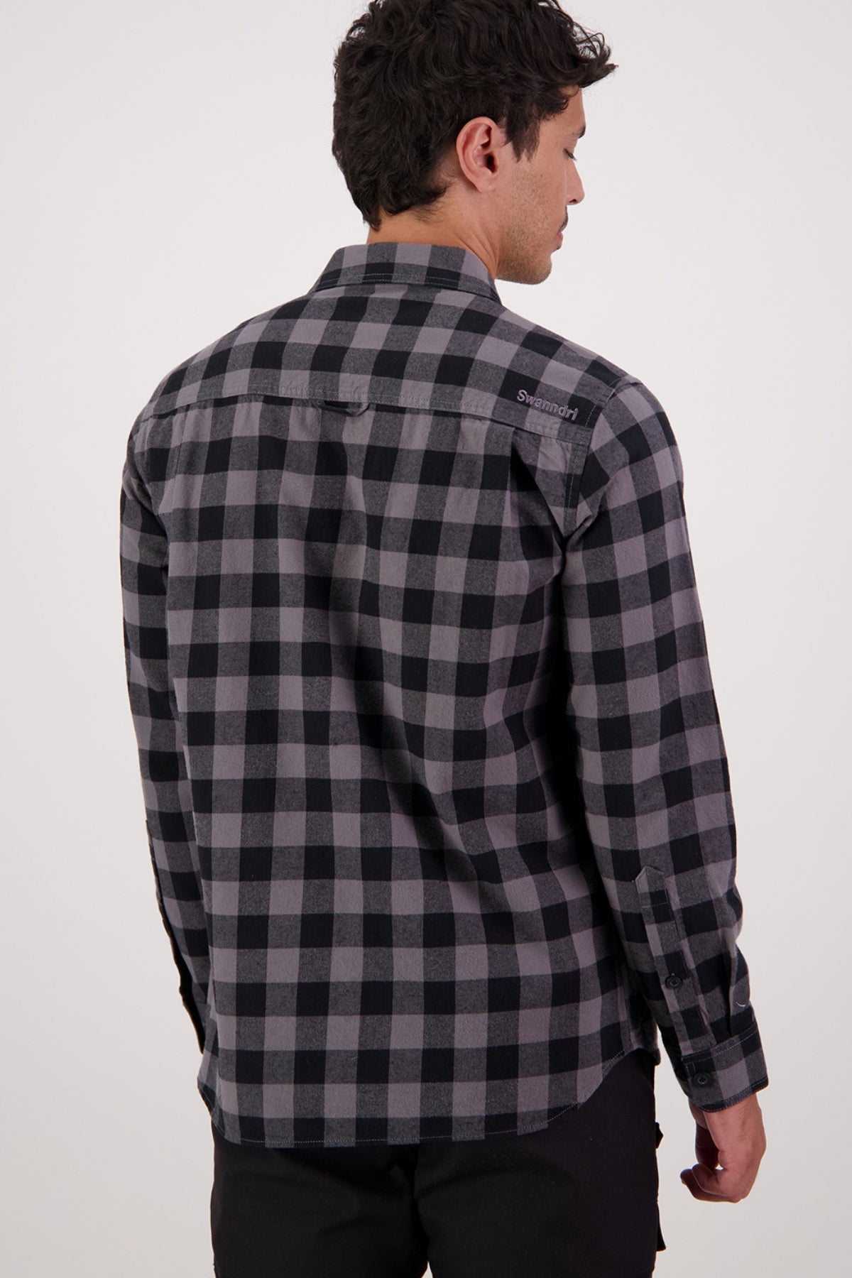 A man is seen from behind wearing the Swanndri Taranaki Tailor Shirt—a black and gray check 100% cotton men's casual shirt—with black pants, standing against a plain white background.