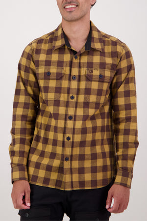 A man in the Swanndri Taranaki Tailor Shirt—a 100% cotton, yellow and brown check-patterned button-up—smiles gently while standing against a plain light backdrop.