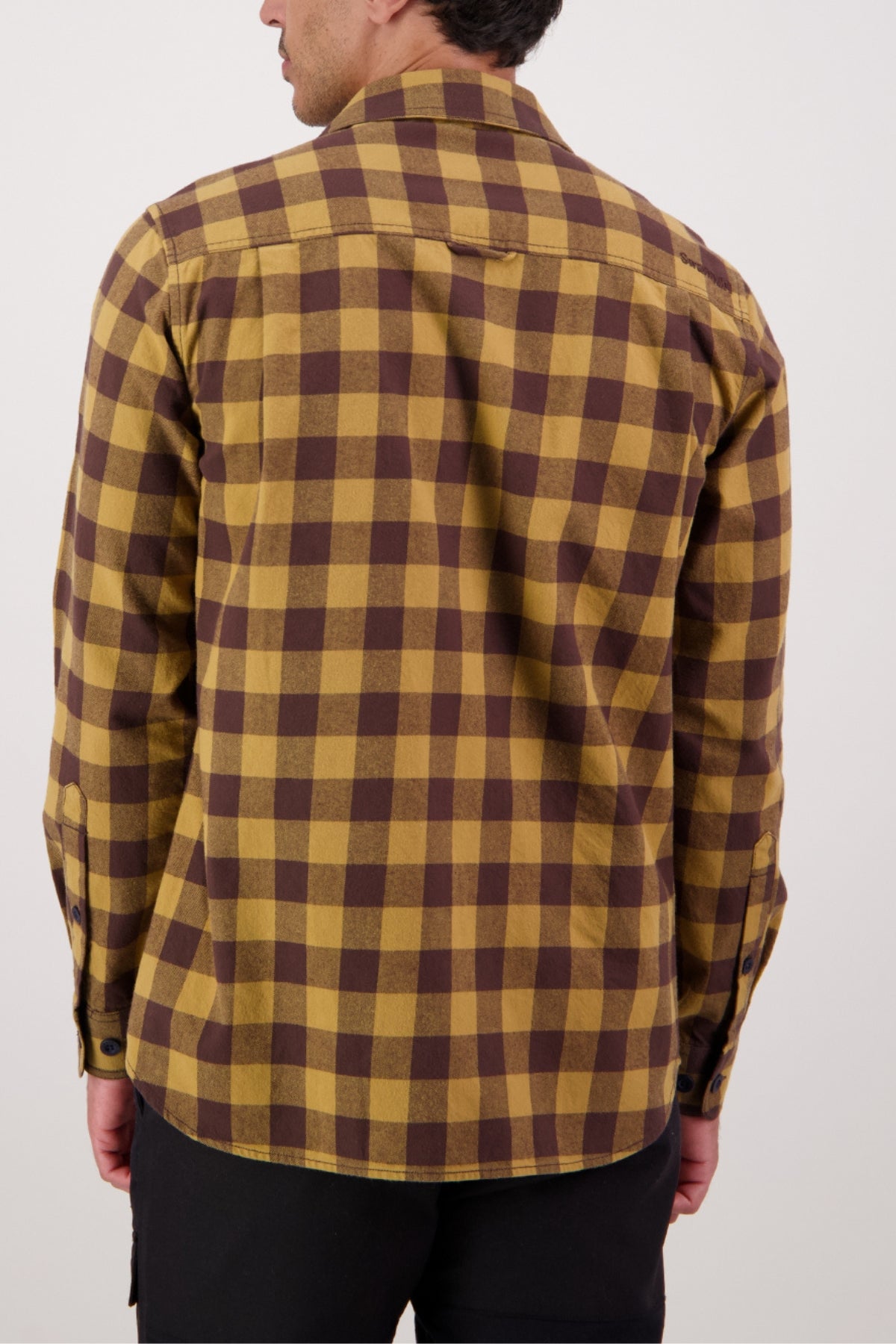 A person is seen from behind wearing the Swanndri Taranaki Tailor Shirt, a long-sleeve yellow and brown check men's cotton button-up, with black pants against a plain white background.