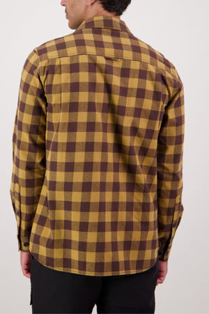 A person is seen from behind wearing the Swanndri Taranaki Tailor Shirt, a long-sleeve yellow and brown check men's cotton button-up, with black pants against a plain white background.