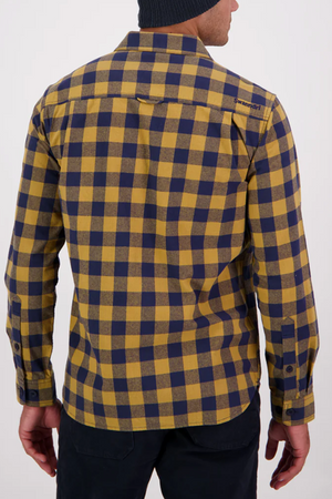 A person in a yellow and navy Swanndri Taranaki Tailor Shirt with buttoned chest pockets and a black beanie stands facing away, highlighting the back of the shirt.
