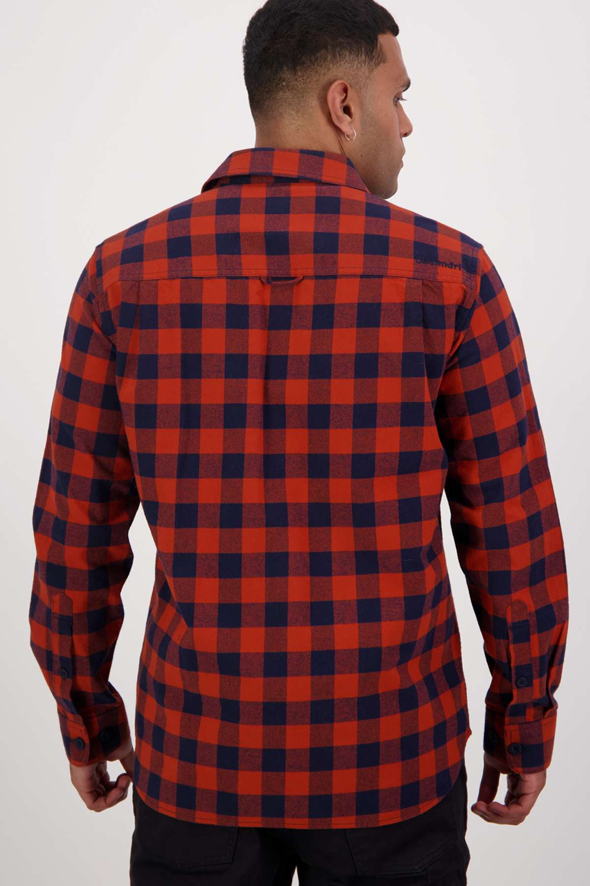 A person with short hair, facing away, wears a Swanndri Taranaki Tailor Shirt—long-sleeved red and blue checkered flannel with a tailored fit—and black pants against a plain white background.