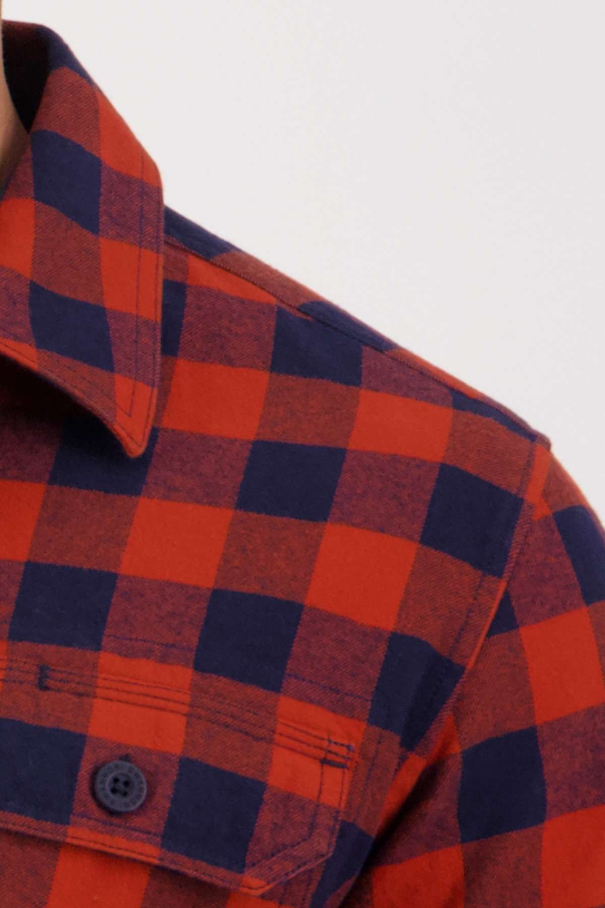 The Swanndri Taranaki Tailor Shirt features a close-up of its red and black checkered flannel design, highlighting the 100% cotton fabric, buttoned collar, and a front pocket with a button, embodying the classic style of this tailored fit piece.