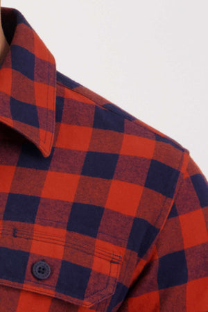 The Swanndri Taranaki Tailor Shirt features a close-up of its red and black checkered flannel design, highlighting the 100% cotton fabric, buttoned collar, and a front pocket with a button, embodying the classic style of this tailored fit piece.