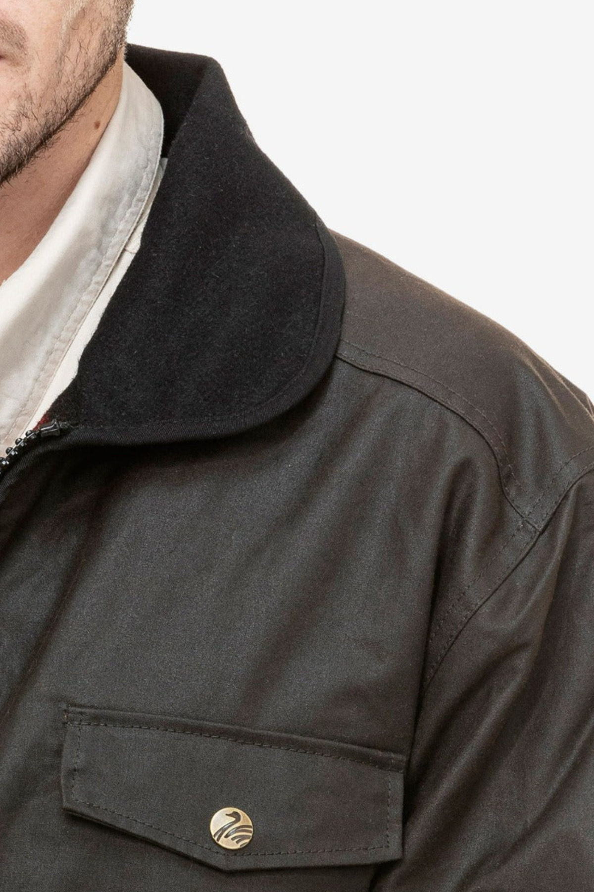 Close-up of a person wearing the Swanndri Waimak Oilskin Jacket, featuring dark waxed cotton, a black collar, and a flap pocket with a round metallic button. Only the lower face and upper torso are visible against a plain white background.