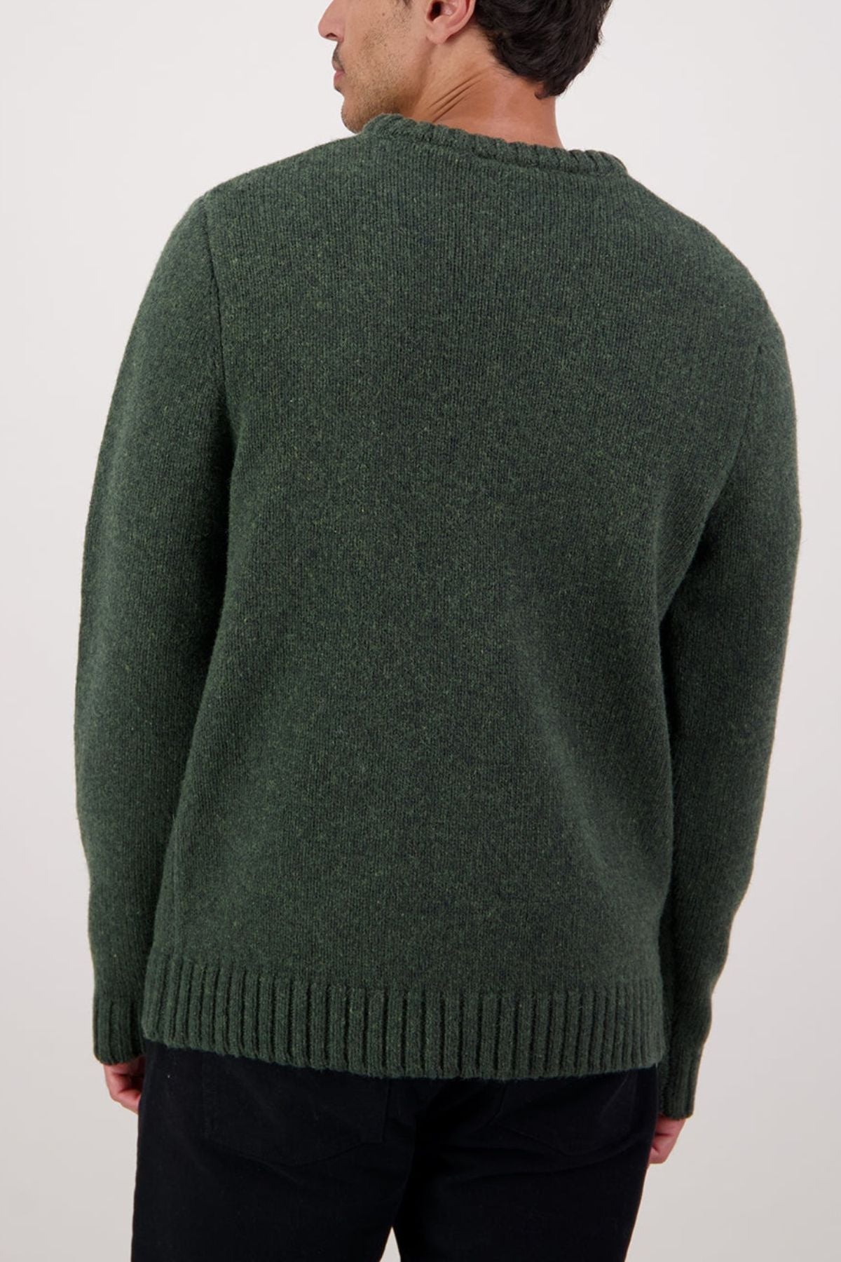 A person is seen from the back wearing a thick, dark green Swaandri Waylins Wool Knit Crew sweater and black pants, standing against a plain light background.